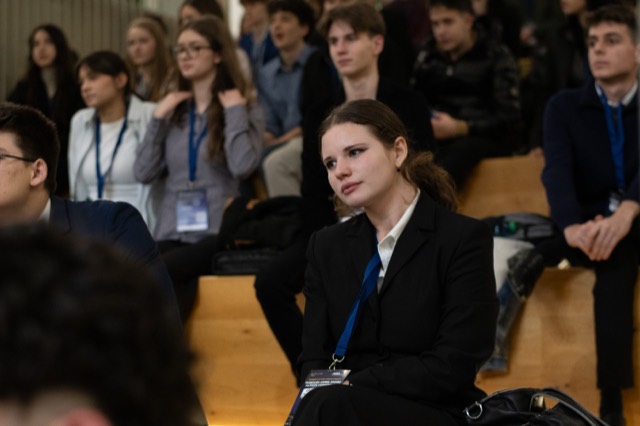 A delegate with a lanyard listens thoughtfully in the audience.