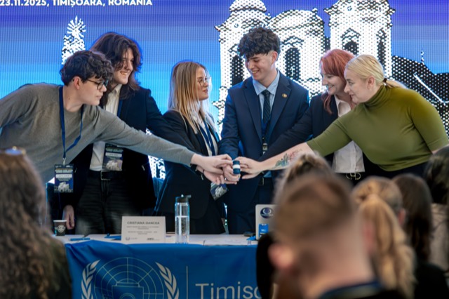 Six organizers stack their hands together in a team cheer over the head table.