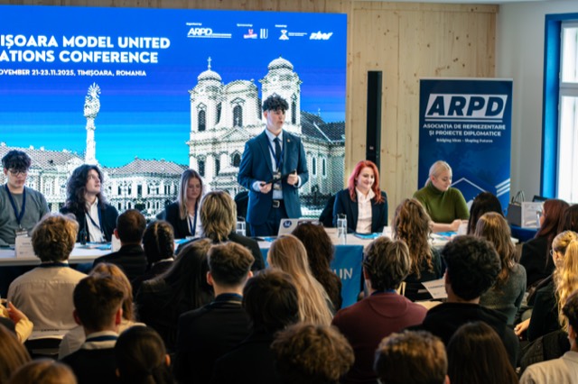The secretariat panel sits beneath the conference title screen as a speaker addresses delegates.