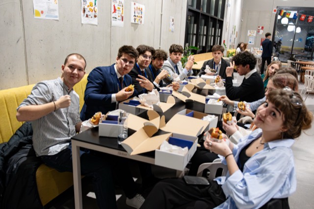 Delegates at a long table hold up burgers and peace signs during the conference dinner.