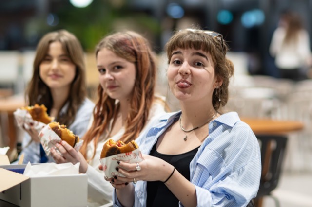 Three girls hold burgers while the nearest playfully sticks out her tongue.