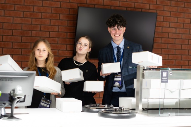 Three organizers pose behind a counter holding white dinner boxes.