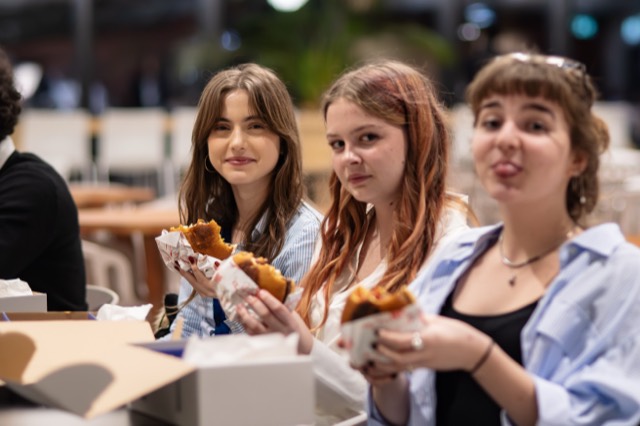 Three delegates smile at the camera holding burgers at the dinner table.