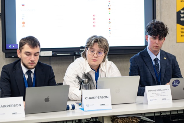 Three student chairs work behind laptops at the committee dais.