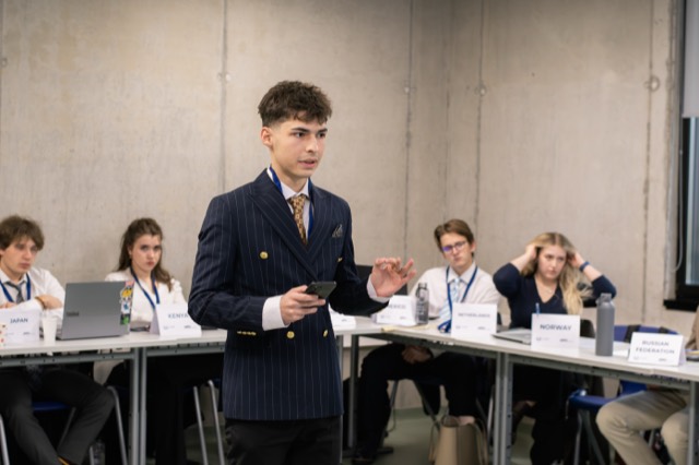 A delegate in a pinstripe blazer stands to address the committee.