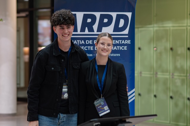 Two smiling organizers stand together behind a lectern in front of the ARPD banner.