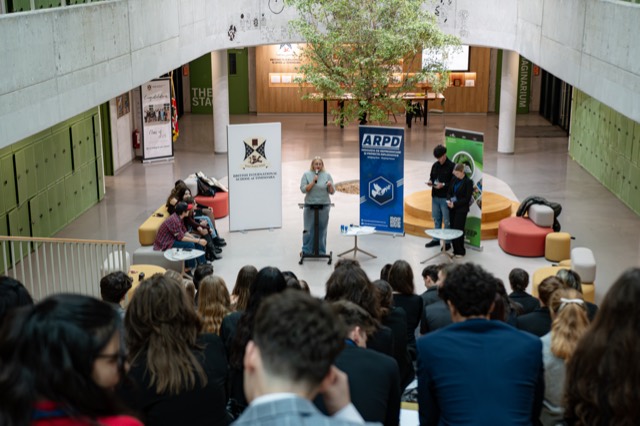 Overhead view of the closing ceremony in the atrium as a speaker addresses the seated audience.