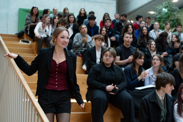 A smiling delegate descends the wooden stairs while the audience watches.