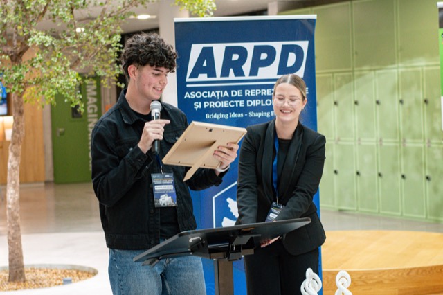 Two co-chairs laugh while announcing awards from the lectern in front of the ARPD banner.