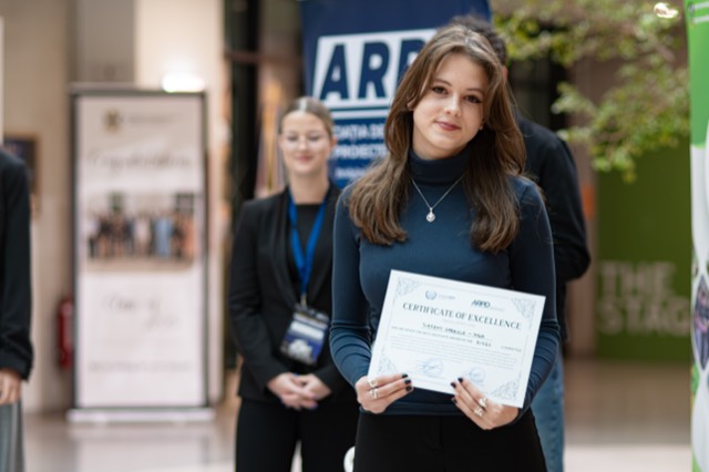 A smiling delegate presents her certificate of excellence to the camera.
