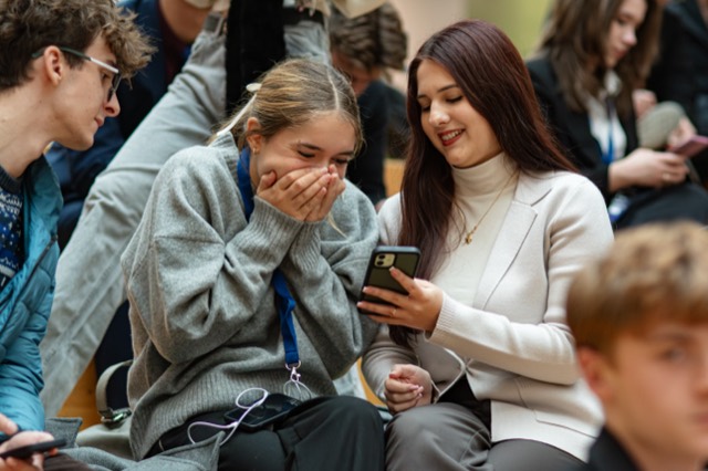 A delegate bursts out laughing as her friend shows her something on a phone.